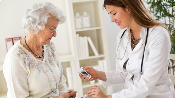 Elderly woman having finger pricked by female doctor to monitor blood glucose.