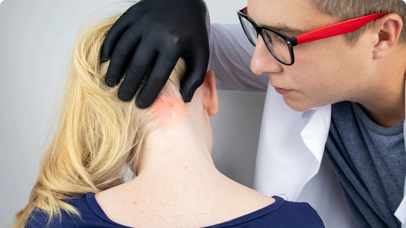 Male doctor inspecting red, scaly skin on the back of a female patient's neck.